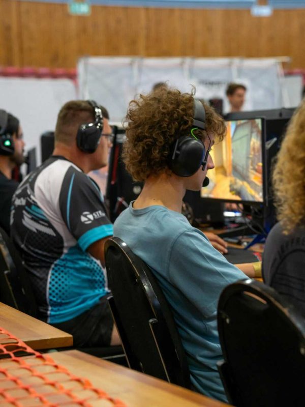 Players wearing headphones focused on video gaming at a competitive esports event indoors.