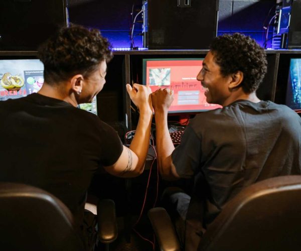 Two male friends enjoying a victory in a gaming competition indoors, showcasing teamwork and friendship.