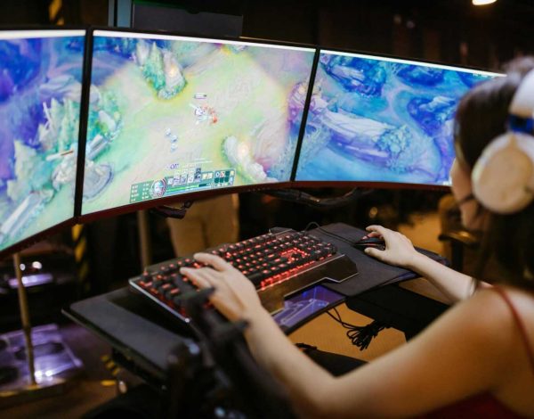 A young woman intently gaming on a multi-screen setup, showcasing vibrant gaming visuals.